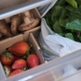 Fresh vegetables and fruits in fidge cabinets. Strawberries, shitake mushrooms and spinach in the vegetable drawer of the opened fridge.