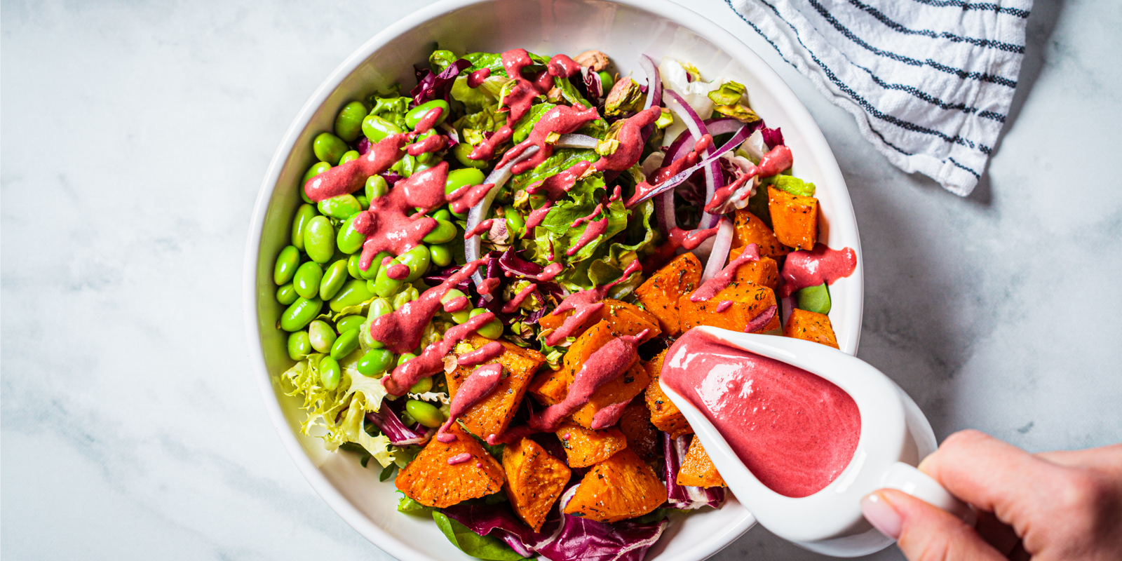 Vegan salad bowl with baked sweet potatoes, edamame beans, nuts and pink beetroot dressing. Vegan food concept.