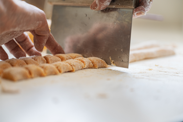 Closeup view of female hands cutting fresh homemade pasta dough to make vegan gnocchi.