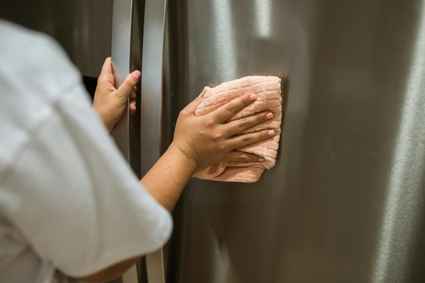 woman cleaning a fridge with a kitchen towel 