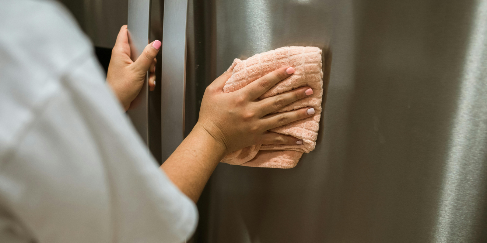 woman cleaning a fridge with a kitchen towel 