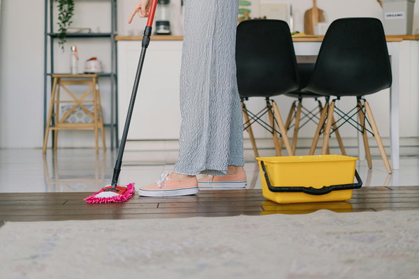 woman using a mop to clean the floor in a brightly lit kitchen, with countertops and cabinets visible in the background