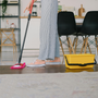 woman using a mop to clean the floor in a brightly lit kitchen, with countertops and cabinets visible in the background