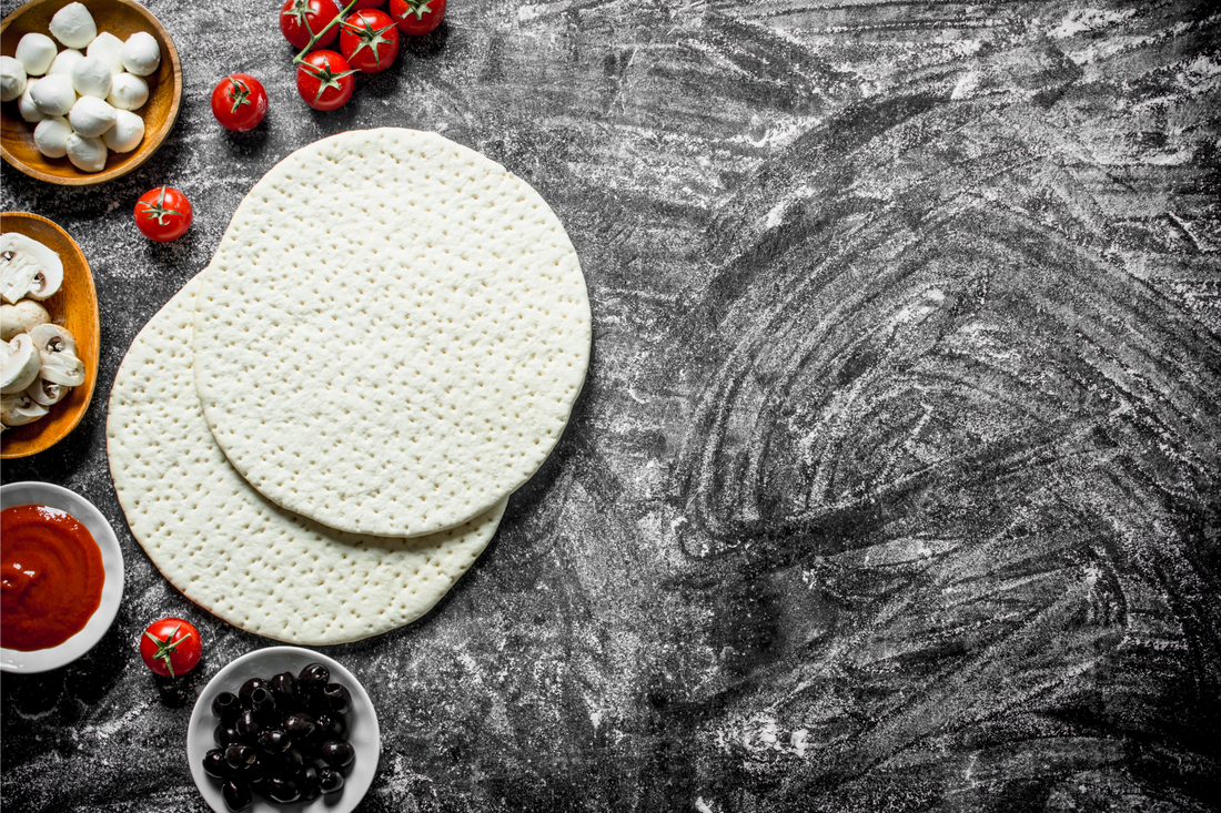 Raw pizza crust on a floured black countertop. Toppings for pizza making and tomato sauce