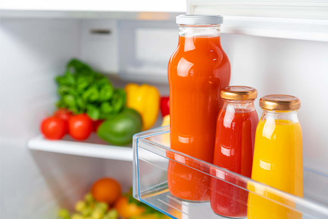 Glass bottle of juice on a fridge shelf, close up. Vegetables in the background.