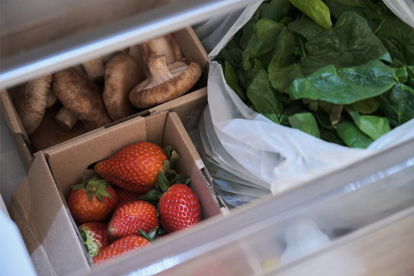 Fresh vegetables and fruits in fidge cabinets. Strawberries, shitake mushrooms and spinach in the vegetable drawer of the opened fridge.