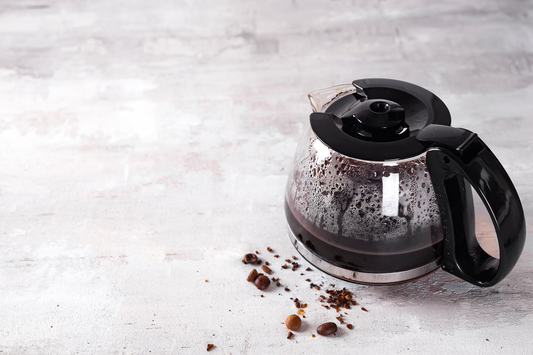 Coffee maker pot filling with coffee beans on a light stone background.