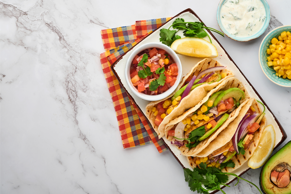 Mexican tacos with grilled chicken, avocado, corn kernels, tomato, onion, cilantro and salsa at white stone table. Traditional Mexican and Latin american street food. Top view.