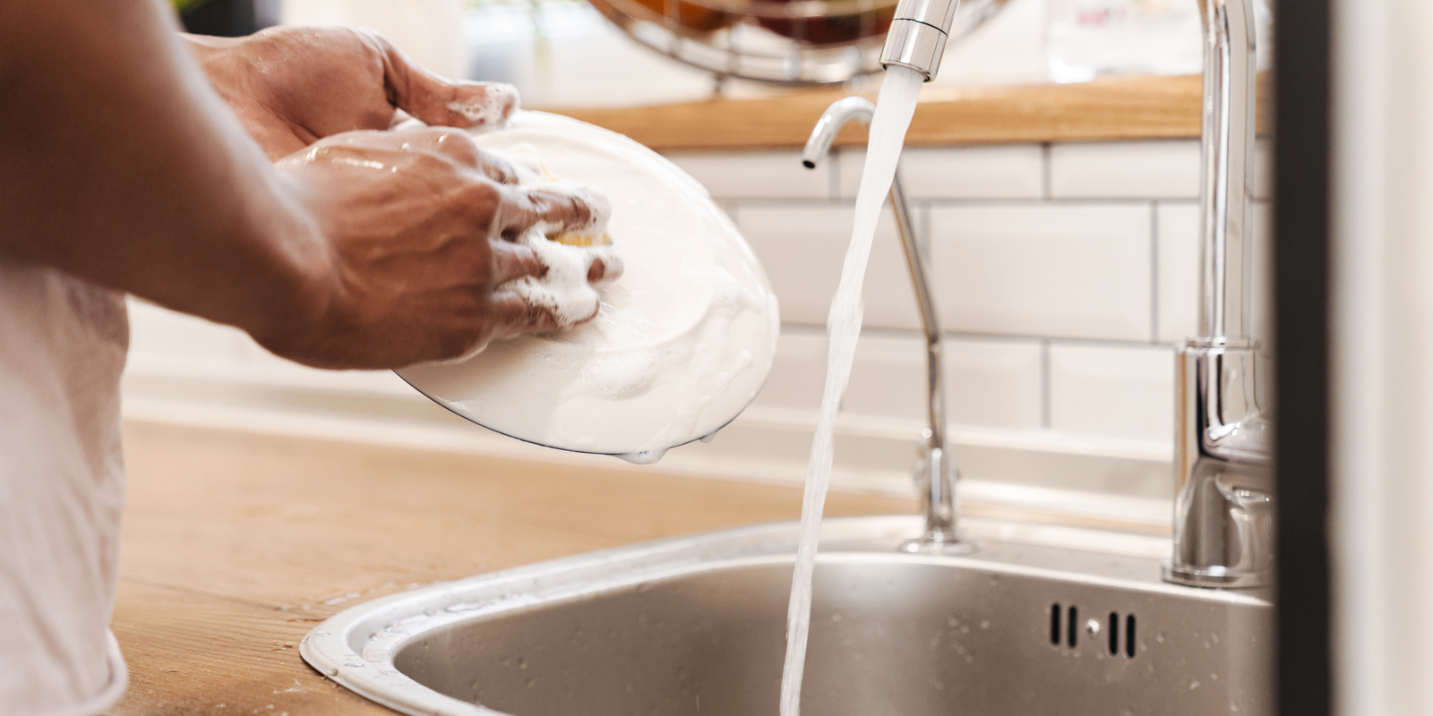 Cropped picture of young african guy in the morning at the kitchen wash the dishes.