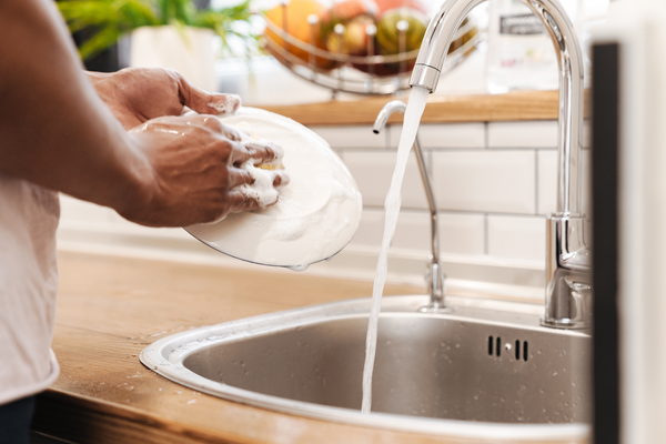 Cropped picture of young african guy in the morning at the kitchen wash the dishes.