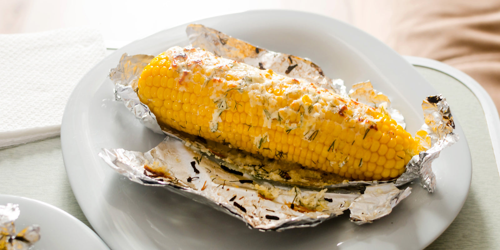 Ears of corn baked with herbs and cheese in foil on plate. Selective focus. Summer food. Ideas for barbecues and grill parties.