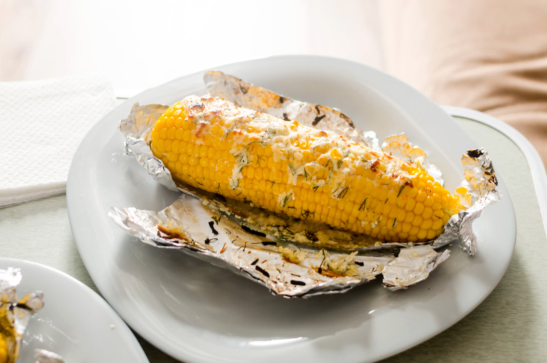 Ears of corn baked with herbs and cheese in foil on plate. Selective focus. Summer food. Ideas for barbecues and grill parties.