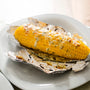 Ears of corn baked with herbs and cheese in foil on plate. Selective focus. Summer food. Ideas for barbecues and grill parties.