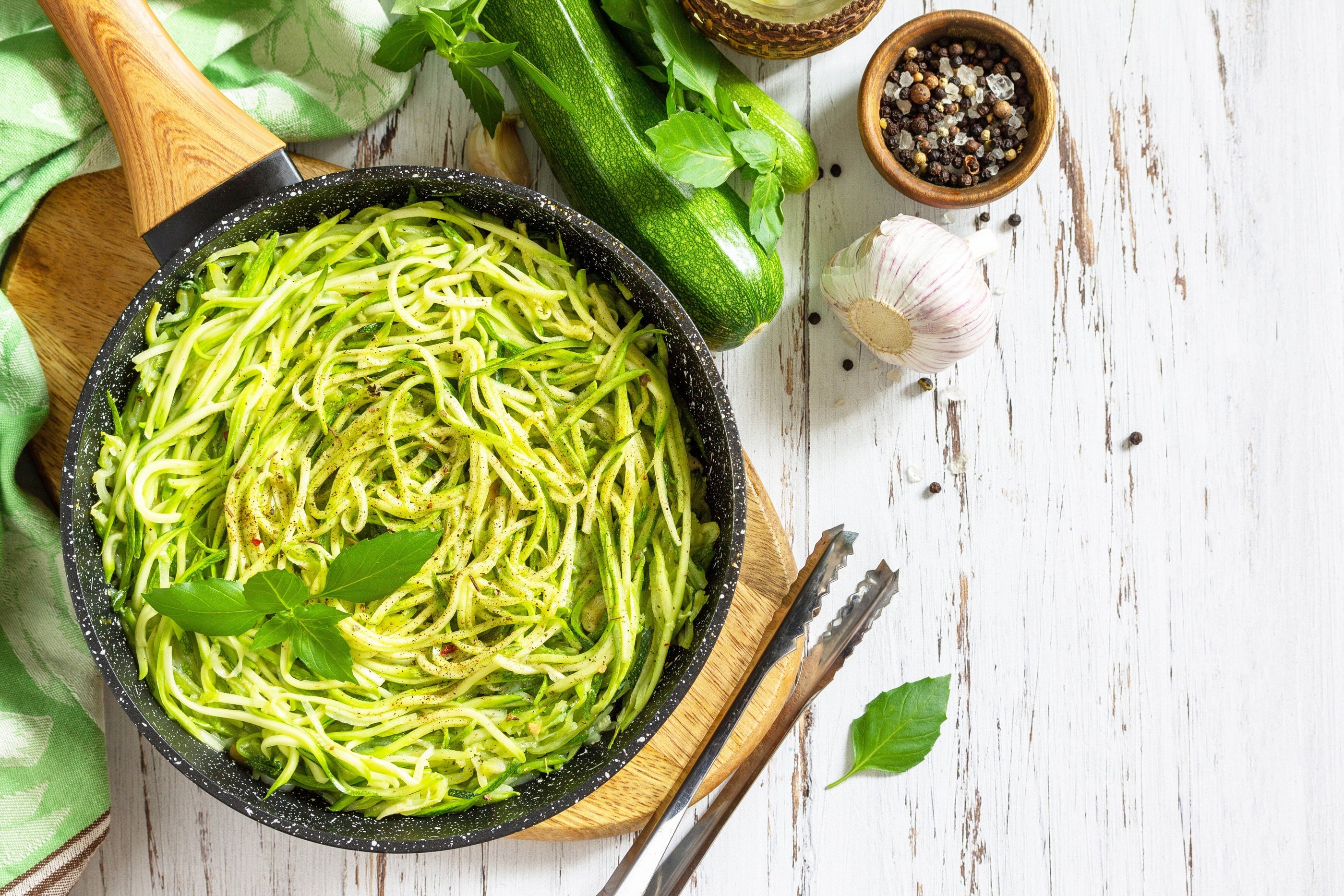 Healthy vegan food, low carb dish. Cooked zucchini noodles with basil and garlic on a rustic wooden table