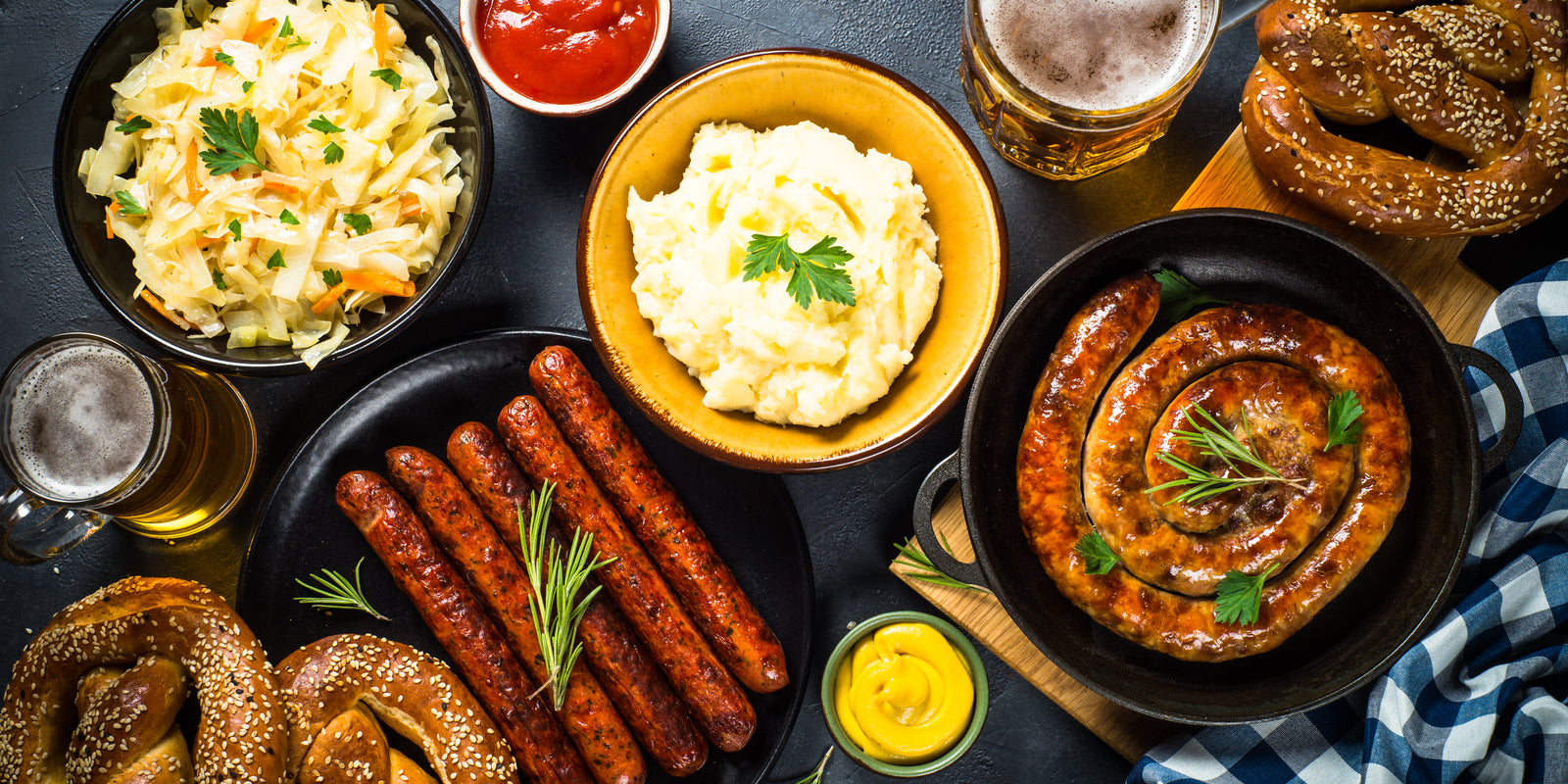 Holiday german dishes - sauerkraut, sausage, pretzel, mashed potato and beer. Top view on black table.