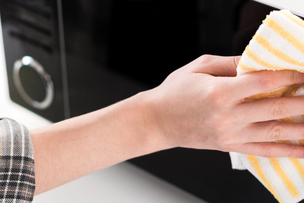 panoramic shot of woman cleaning microwave with rag in kitchen