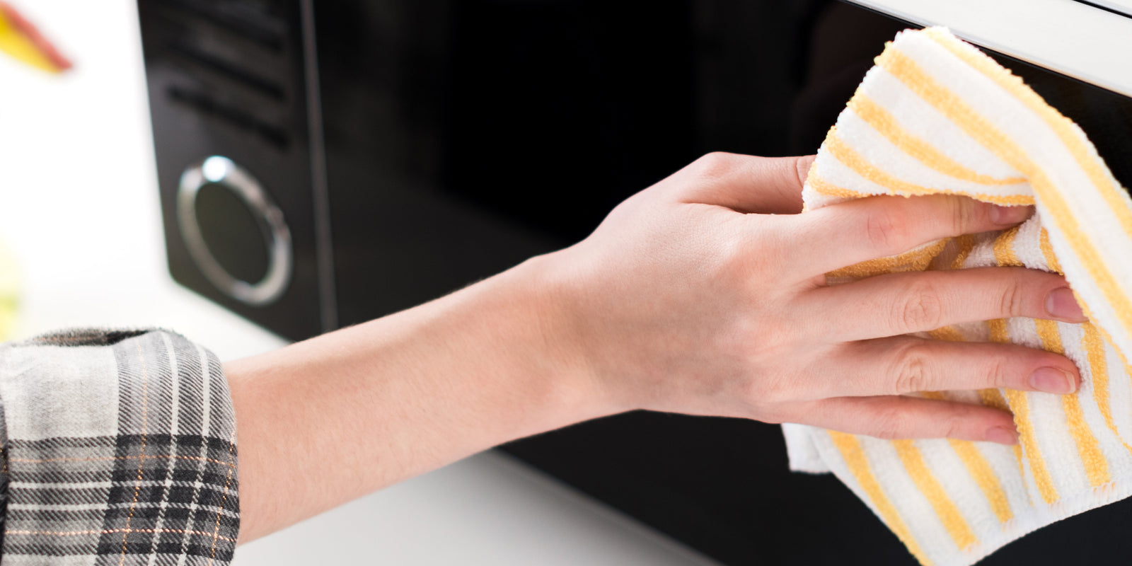 panoramic shot of woman cleaning microwave with rag in kitchen